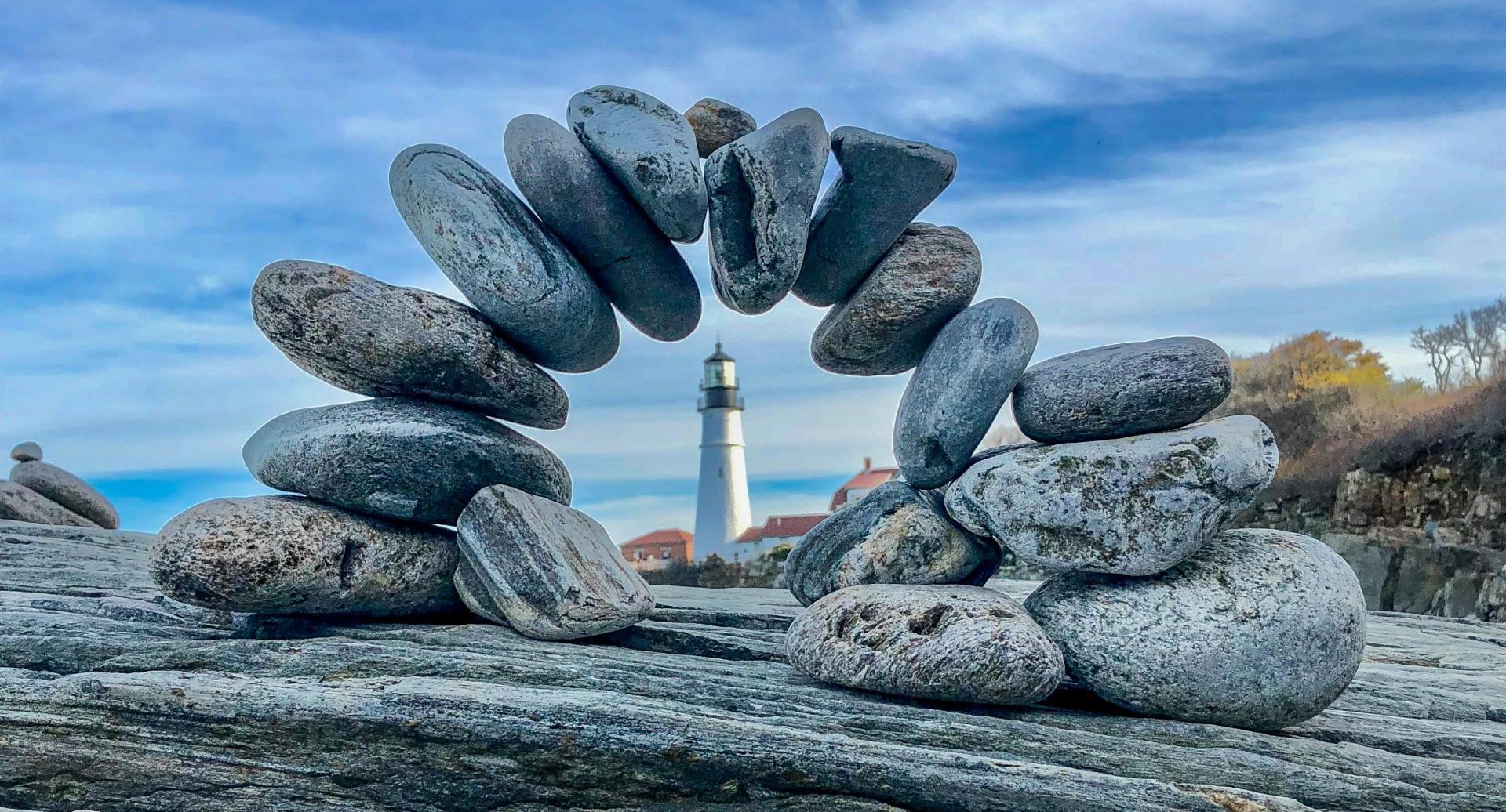 an archway of piled pebbles with a lighthouse in the background